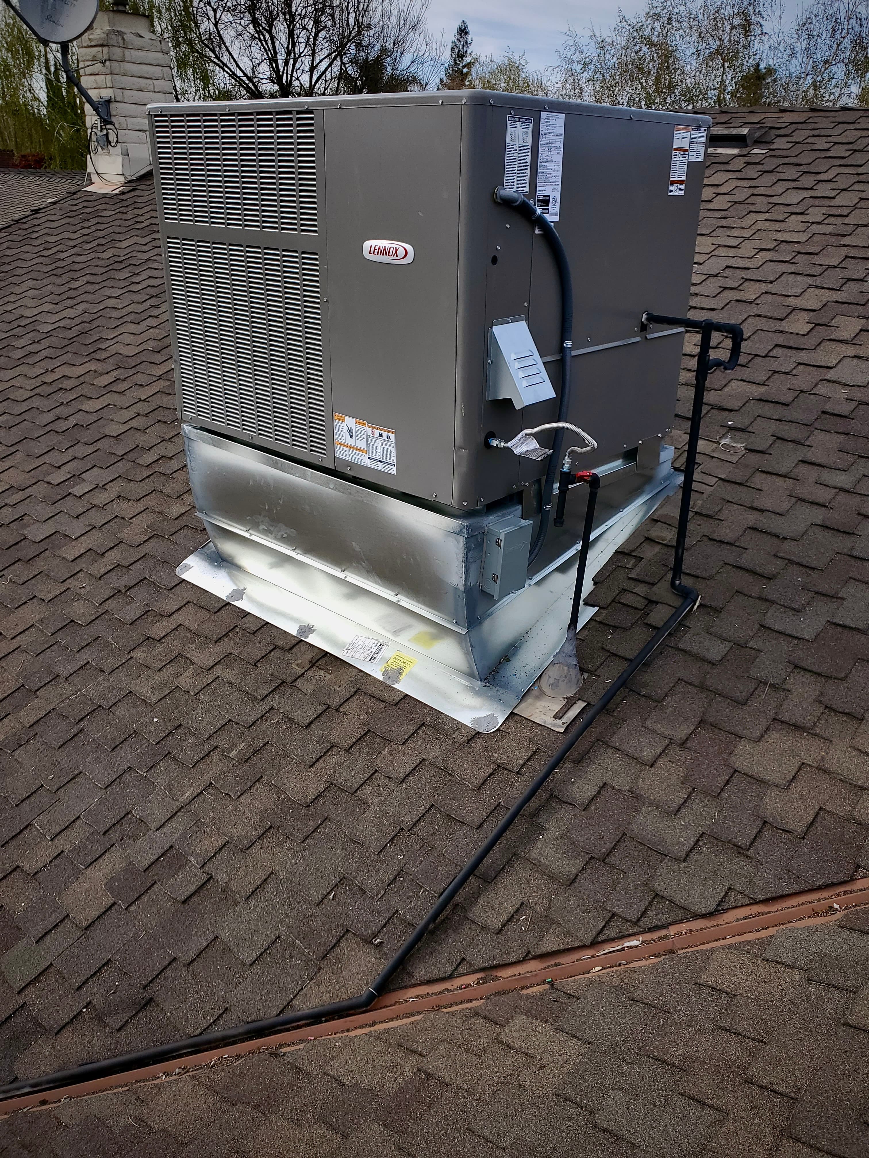 Lennox HVAC unit installed on a brown shingled roof with metal flashing and black pipes.